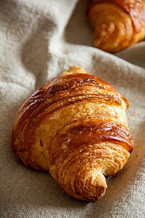 Ein goldbraun glänzendes Croissant mit sichtbaren Schichten liegt auf einem Leinentuch.