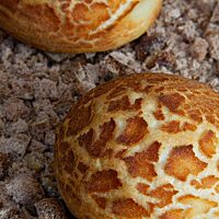 Ein fertig gebackenes Atacama-Brötchen mit rissiger Kruste liegt auf kleinen Brotwürfeln.