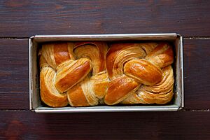 Ein goldgelb ausgebackenes, zu einem Zopf geflochtenes Croissant-Brot mit glänzender Oberfläche liegt in einer Kastenform.