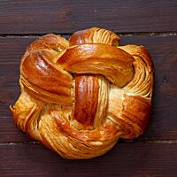 Das verflochtene Croissant-Brot in runder Form liegt auf einem Holztisch.
