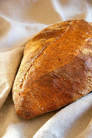 Ein kräftig ausgebackenes, an den Enden spitz zulaufendes Weizenbrot liegt auf einem Leinentuch.