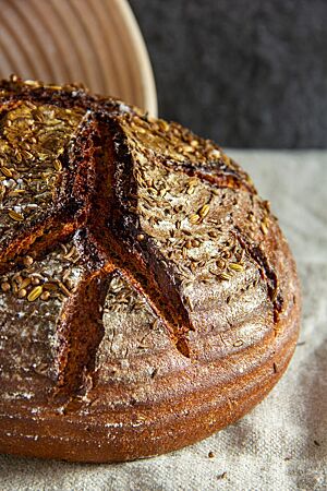 Der dunkel ausgebackene, runde Laib mit glänzender Kruste und rustikalem Ausbund ist mit Brotgewürzen bestreut.