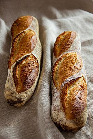 Weißbrot. Zwei Stangenweißbrote mit dem typischen Baguette-Schnitt liegen auf einem Leinentuch.