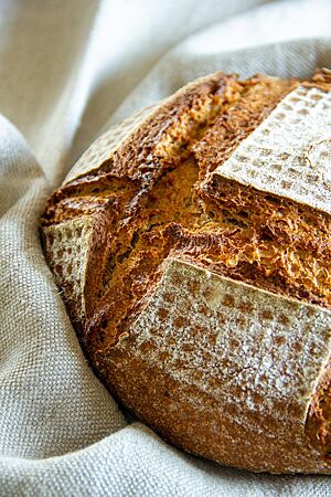 Das kräftig ausgebackene, rustikal aufgerissene Mischbrot mit leicht bemehlter Kruste liegt in einem Leinentuch.