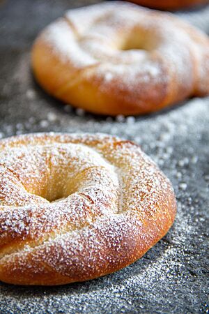 Das mallorquinische Gebäck liegt hellbraun ausgebacken und mit Puderzucker bestreut auf einem dunkelgrauen Steinuntergrund.