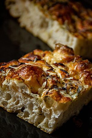 Dinkel-Focaccia. Ein Stück Focaccia mit heller, lockerer Krume ist auf der goldbraunen Kruste mit Kräutern bestreut.
