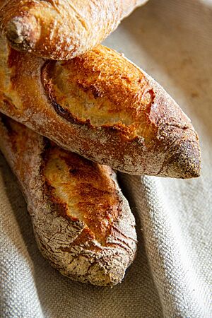 Ein Stapel knusprig ausgebackener Baguettes mit kräftigem Ausbund liegt auf einem hellen Leintuch.