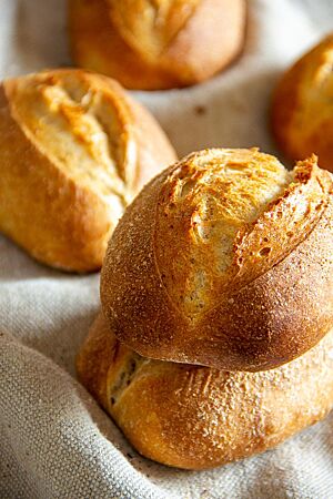 Kartoffel-Dinkelbrötchen. Die goldbraun ausgebackenen Kartoffel-Dinkelbrötchen mit weit geöffnetem Einschnitt liegen auf einem Leinentuch.