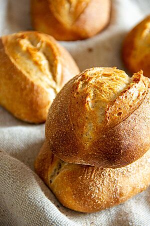 Die goldbraun ausgebackenen Kartoffel-Dinkelbrötchen mit weit geöffnetem Einschnitt liegen auf einem Leinentuch.