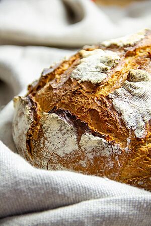 Das rustikal aufgerissene Burebrot mit bemehlter Kruste liegt auf einem Leinentuch.