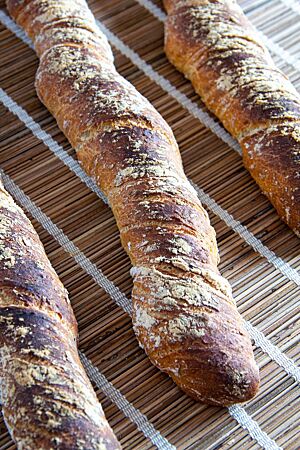 Drei verdrehte Brotstangen mit dunkel ausgebackener, rustikaler Kruste liegen auf einem Tisch.