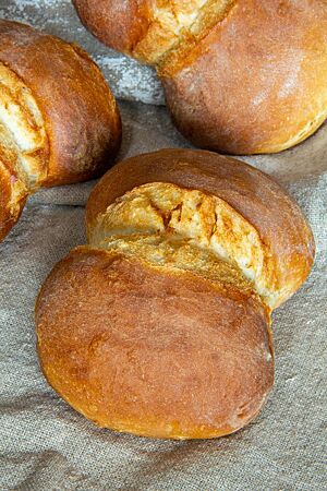 Auf einem Leinentuch liegen die hellbraun ausgebackenen Dresdener Franzsemmeln in Form von Doppelbrötchen mit Querriss an der Anbackstelle.