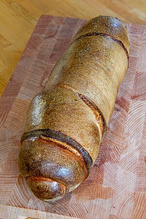 Das kräftig ausgebackene Rollbrot mit glänzender Kruste liegt auf einem Holzbrett.