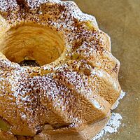 Der Apfel-Biskuit-Kuchen ist goldgelb ausgebacken und mit Puderzucker bestreut.