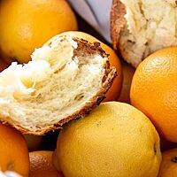 Ein auseinandergebrochenes Stück Brioche liegt auf den Früchten in einer Orangen- und Zitronenkiste und zeigt die langfaserige, sehr luftige Krume.