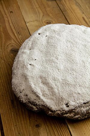 Erzgebirgischer Stollen (2014). Ein flacher, ovaler Stollen mit einer weißen Haube aus Puderzucker liegt auf einem hellen Holztisch.