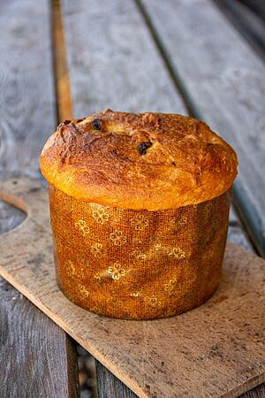 Panettone. Der goldbraun ausgebackene Panettone steht auf einem kleinen Holzbrett.