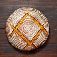 Ein kräftig ausgebackenes Roggenmischbrot mit leicht bemehlter, eingeschnittener Kruste liegt auf einem Holztisch.