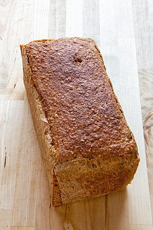 Das in der Kastenform gebackene Wanderbrot mit glatter Kruste liegt auf einem hellen Holztisch.