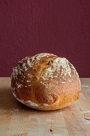 Ein kräftig ausgebackenes Weizenbrot mit leicht bemehlter Kruste liegt auf einem Holztisch.