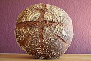 Buttermilchbananenbrot. Das kräftig ausgebackene Buttermilchbananenbrot mit leicht bemehlter Kruste lehnt an einer Wand.