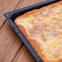 Der dünne, goldgelb bis goldbraun ausgebackene Zuckerkuchen liegt in einem Kuchenblech.