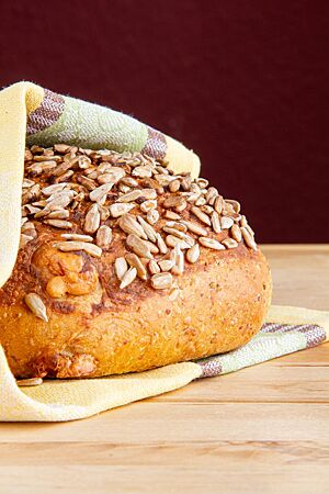Senfbrot. Ein goldbraun ausgebackenes Senfbrot mit Senf und Sonnenblumen auf der Kruste liegt auf einem Holztisch.