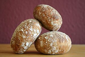 Surdegsfralla med rostad havre (Schwedische Sauerteigbrötchen mit geröstetem Hafer). Die goldbraun ausgebackenen Sauerteigbrötchen mit bemehlter Kruste haben eine glatte Oberfläche.