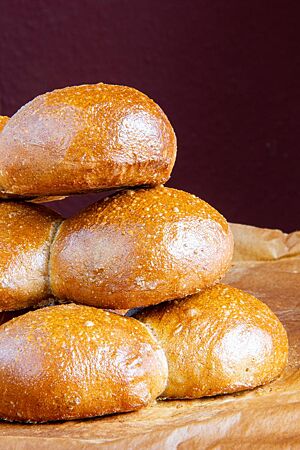 Düsseldorfer Röggelchen. Die goldbraun ausgebackenen Düsseldorfer Röggelchen mit stark glänzender Kruste liegen aufeinander gestapelt auf Backpapier.