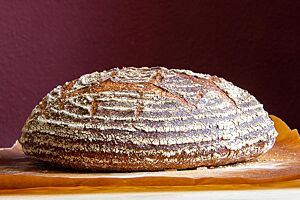 Pain de Campagne-Honfleur. Das kräftig ausgebackene Pain de Campagne-Honfleur mit bemehlter Kruste liegt auf Backpapier.
