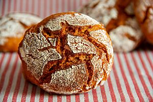 Tomaten-Kartoffel-Brötchen (neu). Ein kräftig ausgebackenes Tomaten-Kartoffel-Brötchen mit rustikal aufgerissener, bemehlter Kruste liegt auf einem gestreiften Tuch.