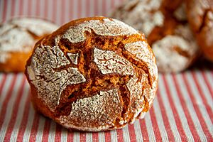 Ein kräftig ausgebackenes Tomaten-Kartoffel-Brötchen mit rustikal aufgerissener, bemehlter Kruste liegt auf einem gestreiften Tuch.