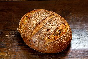 Das goldbraun ausgebackene Rosenkohlbrot mit Sesam auf der Kruste liegt auf einem Holztisch.