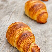 Die Zweikorn-Croissants liegen goldbraun ausgebacken auf einem Holztisch.