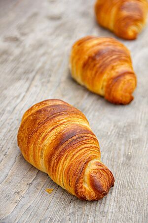 Zweikorn-Croissants. Die Zweikorn-Croissants liegen goldbraun ausgebacken auf einem Holztisch.