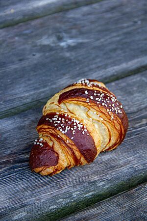 Ein mit Salz bestreutes Laugencroissant aus hellem Mehl liegt auf einem rustikalen Holztisch.