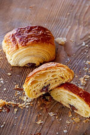 Hüttenplunder (Pain au chocolat). <p>Ein angeschnittenes Pain au chocolat zeigt die mittelporige, elastische Krume und die goldbraun ausgebackene Kruste.</p>