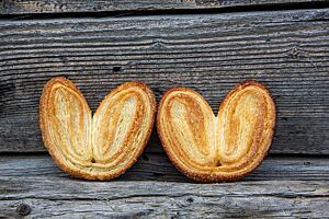 Goldgelb bis goldbraun ausgebackene Schweinsohren lehnen an einer rustikalen Holzwand.