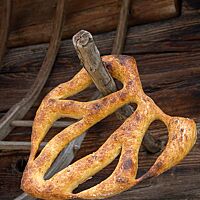 Eine kräftig ausgebackene, schön geformte Fougasse hängt an einem Holzstab vor einer rustikalen Holzwand.