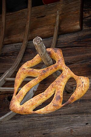 Eine kräftig ausgebackene, schön geformte Fougasse hängt an einem Holzstab vor einer rustikalen Holzwand.