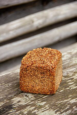 Roggenschrotbrot mit ganzen Körnern. Das kräftig ausgebackene Roggenschrotbrot in Form eines Kastenbrotes liegt auf einem rustikalen Holztisch.