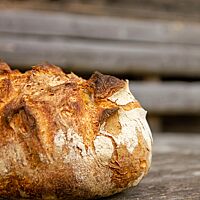 Das kräftig ausgebackene Weizensauerteigbrot liegt auf einem rustikalen Holztisch.