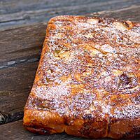Zwanzig aneinandergebackene und mit Puderzucker bestreute Quarkschnecken liegen auf einem rustikalen Holztisch.