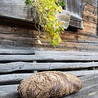 Auf einem Holztisch vor der Almhütte liegt das dunkel ausgebackene Italienische Landbrot mit bemehlter Kruste.