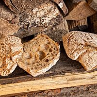 Zwei eckige Weizenmischbrötchen mit bemehlter Kruste liegen auf einem Holzbalken.
