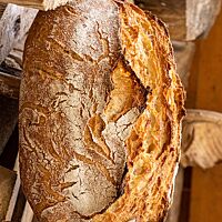 Das Weizensauerteigbrot hat eine knusprig, krosse Kruste und ist aufrecht in einem Holzstapel platziert.