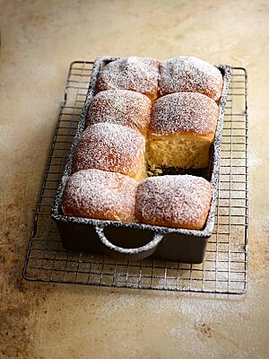 Die mit Puderzucker bestreuten Buchteln wurden angeschoben in einer Auflaufform gebacken und haben eine dünne, glatte Kruste und eine helle, fluffige Krume.