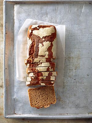 Das in der Kastenform gebackene Roggenvollkornbrot mit weiß bemehlter, rustikaler Kruste liegt auf einem Backblech und zeigt im Anschnitt seine dunkle, kleinporige Krume.