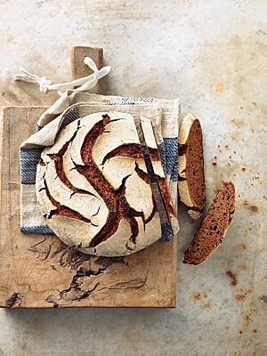 Der Kontrast zwischen der weiß bemehlten, rustikal aufgerissenen Kruste und der dunklen, kleinporigen Krume ist beim Roggenschokobrot besonders stark ausgeprägt.