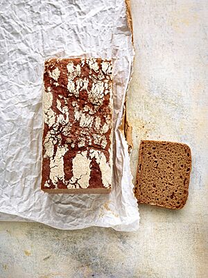 Das Dreikornvollkornbrot wurde in einer Kastenform gebacken und hat eine fein gemaserte, weiß bemehlte Kruste und eine dunkelbraune, lockere Krume.
